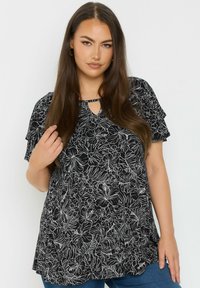 Blusa nera con motivi floreali bianchi, maniche corte a sbuffo, scollatura a chiave e vestibilità morbida, realizzata in tessuto leggero.