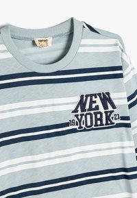 Gestreiftes Langarm-T-Shirt in Hellblau, Dunkelblau und Weiß. Strukturiertes Patch "NEW YORK 19 21" auf der Brust. Gerippter Rundhalsausschnitt. Baumwollmaterial.