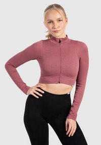 Korte lange mouwen top in geribbeld rozenstof met een hoge hals en een voorzijde ritssluiting, gecombineerd met zwarte high-waisted leggings.