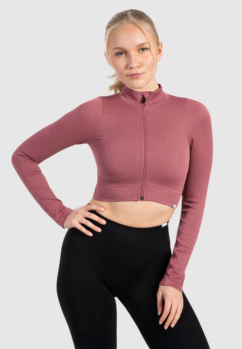 Korte lange mouwen top in geribbeld rozenstof met een hoge hals en een voorzijde ritssluiting, gecombineerd met zwarte high-waisted leggings.
