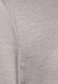 Jasnoszara tkanina dzianinowa o miękkim, teksturowanym wykończeniu i prostym wzorze. Charakteryzuje się gładkim przejściem przy szwie ramion.