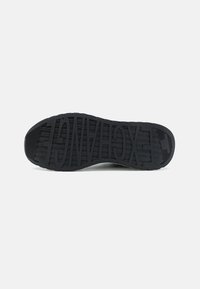 Semelle de chaussure noire en caoutchouc texturé, présentant un logo en relief, avec des motifs de semelle circulaires et rectangulaires pour une adhérence accrue.
