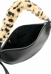 Sac à main en cuir noir avec une fermeture éclair ouverte montrant un intérieur vide et une anse en tissu beige à pois noirs et duveteux.