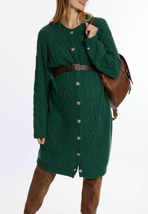 Green knitted cardigan dress with cable pattern, gold buttons, and ribbed cuffs, cinched at the waist with a brown belt.