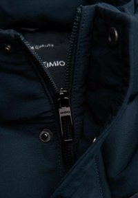 Mörkblå isolerad jacka med dragkedja, som har en silverfärgad dragflik och tryckknappar, vilket framhäver den släta texturen och sömmarna.