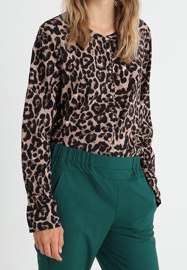 Leopardenmuster-Bluse aus glattem Stoff mit durchgehender Knopfleiste und langen Ärmeln, kombiniert mit grünen hochtaillierten Hosen.