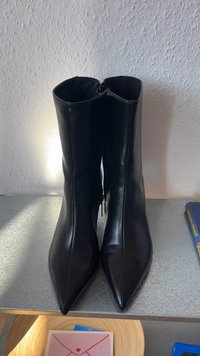 Črne usnjene gležnjače s koničastim nosom in zadrgo na hrbtni strani. Gladka tekstura, minimalistična zasnova in visok ščit.