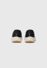Chaussures de sport noires avec un tissu texturé, des accents élastiques et une semelle intercalaire blanche. La semelle extérieure est en caoutchouc avec un motif en zigzag pour une meilleure adhérence.