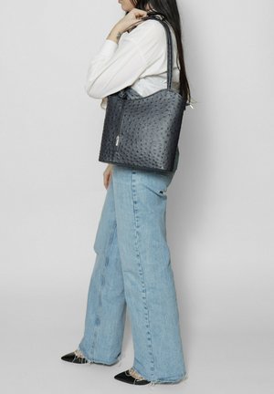 Donkergrijze leren tote bag met een gestructureerd oppervlak, voorzien van een ritssluiting en lange hengsels, gecombineerd met lichtblauwe wijde jeans.