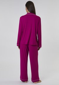 Långärmad, fuchsia pyjamasuppsättning med vit passpoal, med knappad krage och löst sittande byxor, tillverkad av mjukt och lätt material.