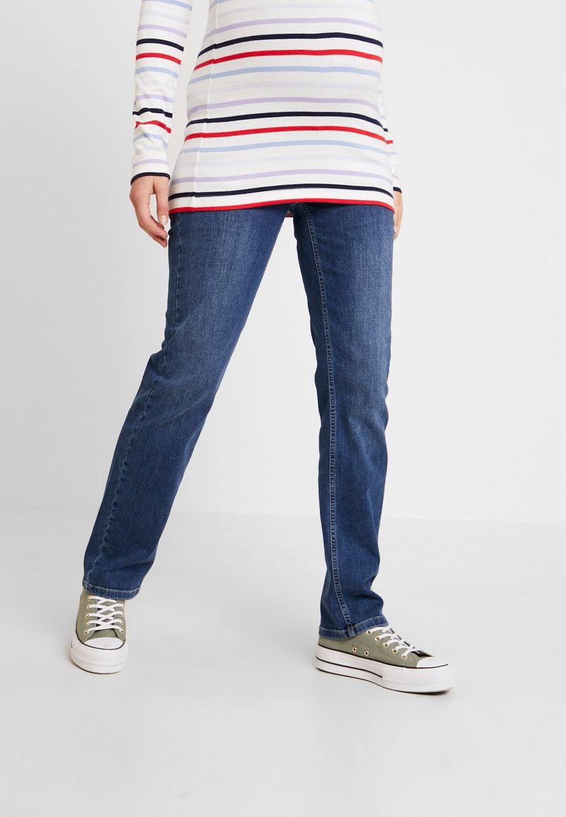 Jean droit bleu en denim, associé à des baskets vert clair et blanches. Haut à rayures à manches longues avec des couleurs variées (rouge, bleu, rose).