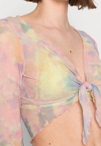 Gennemsigtig, pastelfarvet top med knytefront og et akvarelmønster i nuancer af pink, gul og grøn. Har en delikat blondekant og flagrende kanter.