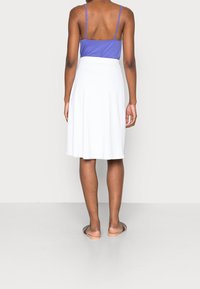 Biała spódnica w kształcie dzwonu o gładkiej fakturze, noszona na niebieskim topie na ramiączkach. Ma wysoki stan i prosty design, sięgająca do połowy łydki.