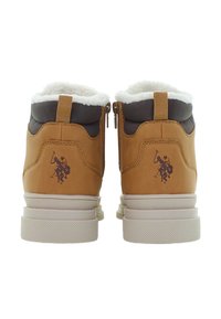 Hnědé zimní boty s bílou fleecovou podšívkou, bočními zipy a tmavým logem hráče póla na koni vzadu.