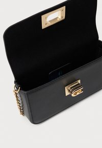 Bolso cruzado de cuero negro con cadena dorada y cierre, abierto para mostrar el interior negro liso y un pequeño bolsillo en el interior.