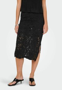 Schwarzer Spitzenrock mit Blumenmuster, knielang, mit seitlichen Schlitzen, kombiniert mit schwarzen offenen Schuhen. Glatte Textur und detailliertes Design.