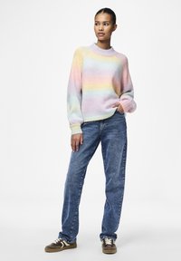 Pastel gradient trui met een ronde hals en ribbelmanchetten, gedragen met losvallende blauwe denim jeans en bruine sneakers met witte accenten.