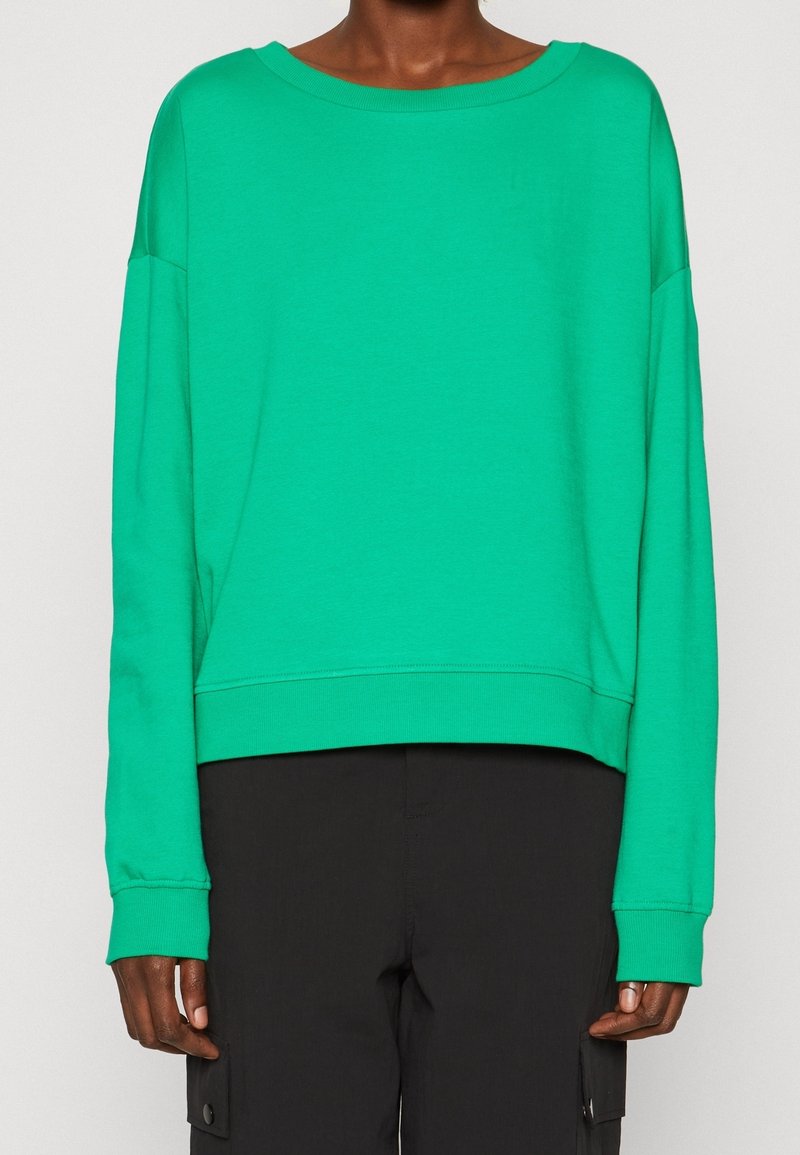 Sudadera verde, corta, con mangas largas y escote ancho. Fabricada en un material suave, con una textura lisa y puños acanalados.