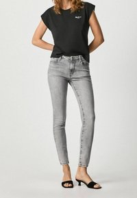 Svart t-shirt med kort ärm och en liten vit logotyp, matchad med ljusgrå skinny jeans och svarta öppna klacksandaler.