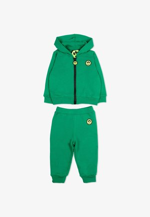 Ensemble sweat à capuche et pantalon taille bébé vert avec des patchs de visage souriant jaune sur la poitrine, la tirette de la fermeture éclair et la poche, posé à plat sur fond blanc.