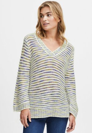 Pull rayé vert, lavande et blanc. Design à encolure en V avec des manches ballon, texture côtelée et coupe casual. Porté avec un jean bleu.