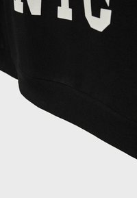 Tissu noir avec ourlet côtelé et grandes lettres blanches partielles imprimées sur la partie supérieure, probablement une partie d'un vêtement comme un sweat-shirt.