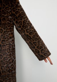 Cappotto in pelliccia finta con stampa leopardata, caratterizzato da maniche lunghe e una consistenza morbida, prevalentemente marrone con accenti marrone scuro, che si estende fino al polso.