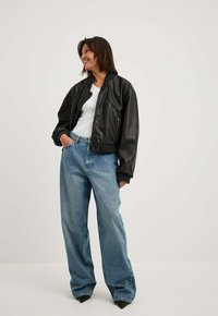 Juodas odinis bomberis su užtrauktuku priekyje, guminėmis rankovėmis ir laisvu siluetu, derinamas su aukštu juosmeniu ir laisvomis mėlynomis džinsinėmis kelnėmis.