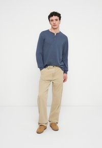 Μπλε πουκάμισο henley με μακριά μανίκια και τρία κουμπιά στη λαιμόκοψη, σε συνδυασμό με ανοιχτό μπεζ παντελόνια από κορντονέ και καφέ αθλητικά παπούτσια. Απλή, άνετη γραμμή.