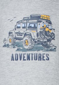 Grijze T-shirt met een afbeelding van een robuust off-road voertuig met een motor erop. De tekst luidt "AVONTUREN" in vetgedrukte letters.