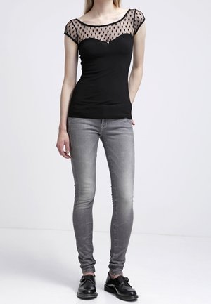 Top negro con superposición de puntos transparentes, diseño ajustado y escote redondeado. Combinado con pantalones skinny gris descoloridos y calzado negro.