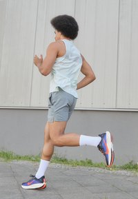 Sportstøj bestående af en lysegrøn ærmeløs top med striber, grå shorts og sorte, orange og blå løbesko med hvide sokker.