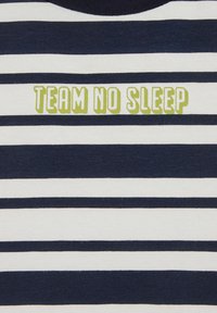 Bombažna majica z mornarsko modrimi in belimi vodoravnimi črtami ter besedilom "TEAM NO SLEEP" v svetlo zeleni barvi in okrogli pisavi na sredini.