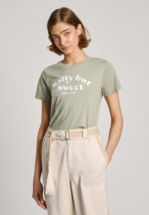 Ljusgrön bomullströja med texten "Salty but Sweet" i vitt, kombinerad med högmidjade beige byxor med knytbälte.