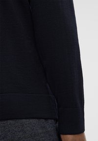 Granatowy sweter z ściągaczem przy mankietach i u dołu, wykonany z dzianiny o fakturze. Konstrukcja zapewnia bezszwowe przejście od rękawa do korpusu.