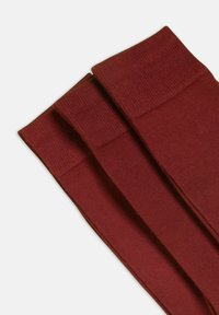 Calzini rossi a coste con una superficie liscia, piegati per mettere in mostra i loro polsini elasticizzati e la forma. Progettati per comfort e durata.