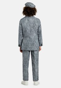 Completo in misto lana grigio e bianco con giacca lunga e pantaloni dritti, abbinato a un berretto coordinato. Sneakers bianche indossate.