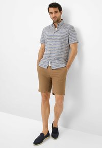 Chemise à manches courtes, col avec un motif géométrique bleu et blanc, associée à un short beige. Chaussures : mocassins navy.