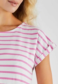Bavlněné tričko s bílým podkladem a tenkými růžovými vodorovnými pruhy. Má lodičkový výstřih a krátké ohrnuté rukávy. Hladká textura.