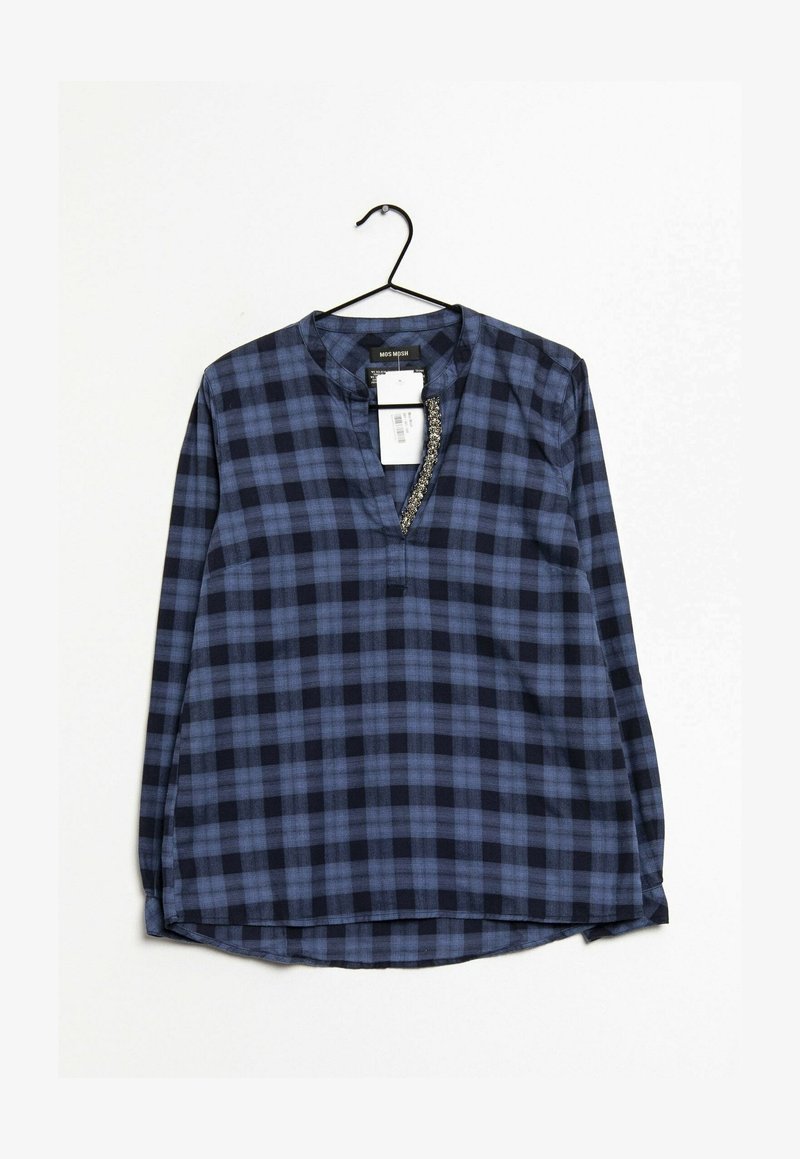 Blouse à manches longues à carreaux bleus et noirs avec un col en V et un détail décoratif le long de l'encolure, suspendue sur un cintre noir.
