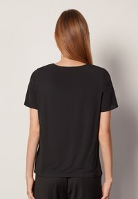 Svart kortärmad topp med avslappnad passform, rund halsringning och slät textur. Sömmar på axlarna och sprund på sidorna av fållen.