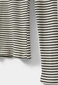 Maglietta a maniche lunghe a righe bianche e nere con orlo arrotondato. Le righe sono distanziate uniformemente, creando un aspetto strutturato.