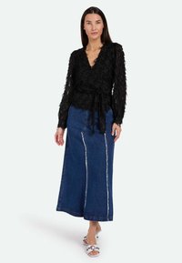 Top negro transparente con patrón floral texturizado, combinado con una falda maxi de mezclilla con una costura en el frente. Sandalias blancas deslizantes completan el look.