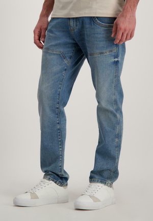 Lichtblauwe spijkerbroek met een rechte snit, voorzien van voorkruiden en subtiele vervaging, gecombineerd met witte sneakers met grijze accenten.