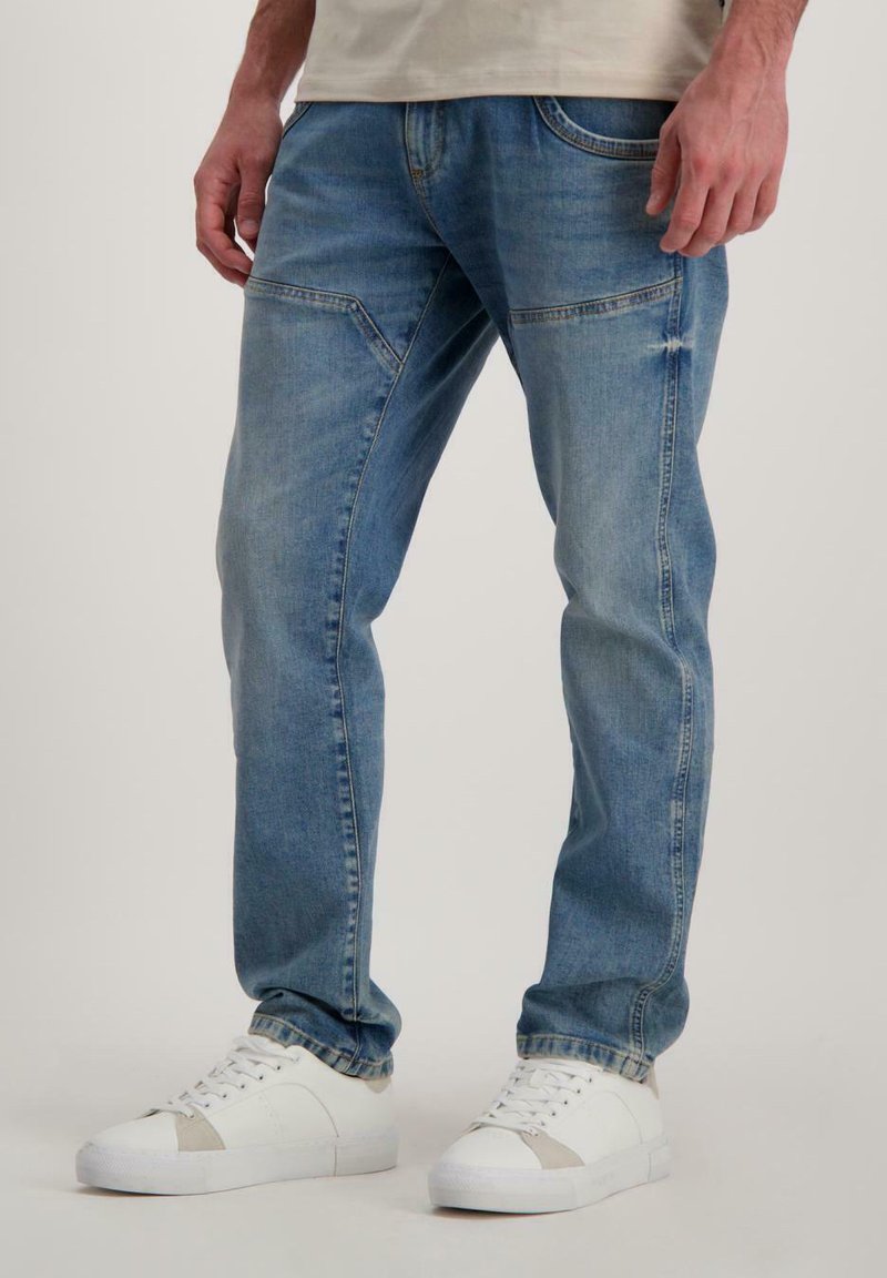 Lichtblauwe spijkerbroek met een rechte snit, voorzien van voorkruiden en subtiele vervaging, gecombineerd met witte sneakers met grijze accenten.