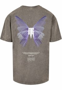 Grå oversized t-shirt med et lilla sommerfugl grafik på ryggen, med et hvidt logo og teksturerede stofdetaljer.