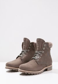 Bottines en cuir marron avec des lacets gris, un col en fausse fourrure, des œillets en métal et une semelle en caoutchouc texturée ; marquées sur les côtés.