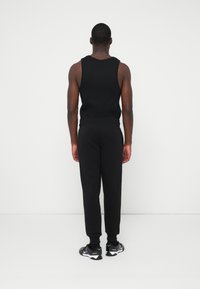 Un maiou negru fără mâneci și pantaloni joggers asortați, ambele dintr-un material neted și elastic. Pantofi sport cu talpă albă. Design simplu, minimalist.
