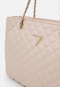 Sac fourre-tout beige matelassé en matériau synthétique brillant, arborant un logo en triangle doré et deux anses en chaîne.