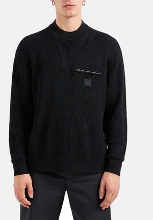 Maglione nero a maglia con collo alto, texture a coste e tasca sul petto con zip. Presenta una piccola etichetta del logo sulla tasca.